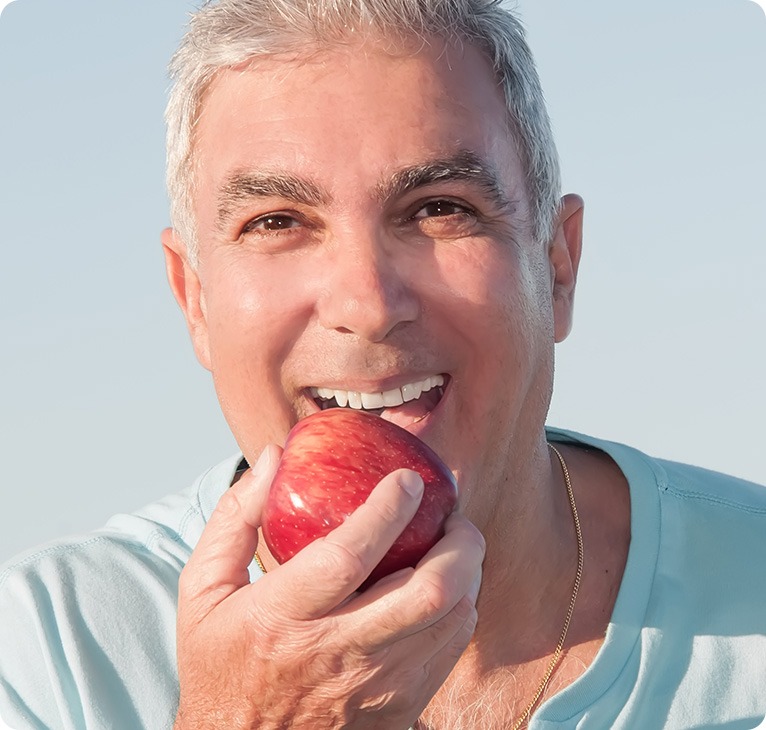 Patient Eating Apple With Dentures | Chestermere Lifepath Dental | Lifepath Dental & Wellness